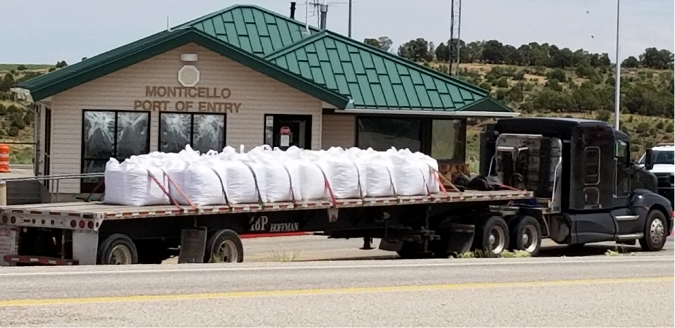 Truck pulling flatbed trailer loaded with white bags crossing in front of the Monticello Port of Entry